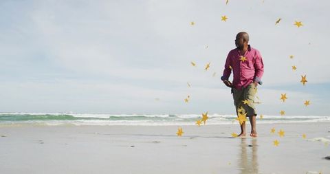 Standing barefoot man wearing pink shirt and olive shorts on beach with gold star confetti