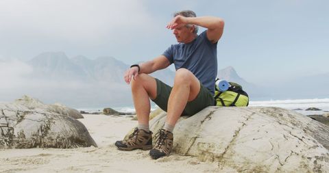 Senior Hiker Resting on Beach Rock Using Smartwatch