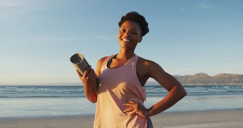 Smiling woman with yoga mat on beach at sunset