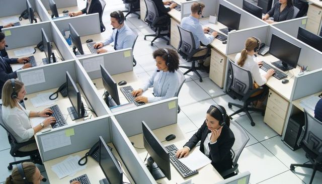 Customer service agents working in busy open-plan call center cubicles with headsets