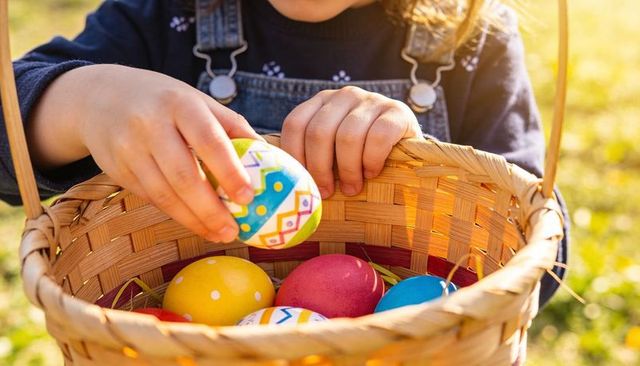Child collecting colorful easter eggs in wicker basket outdoors during golden hour