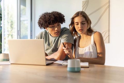 Young couple collaborating at home with laptop and notebook in sunlit minimalist kitchen