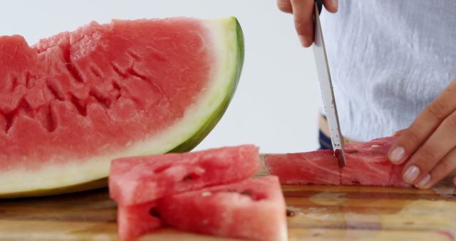 Person slicing a ripe watermelon on a wooden cutting board. Ideal for depicting healthy eating, fresh fruit consumption, summer refreshments, cooking tutorials, or food preparation scenes. Useful for blogs, advertisements, and social media posts on nutrition, diet, and summer themes.