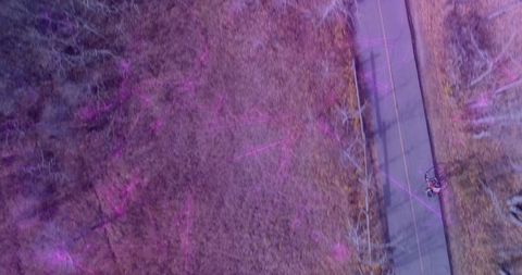 Aerial cycling teen in red jacket riding on rural paved path with purple light streaks