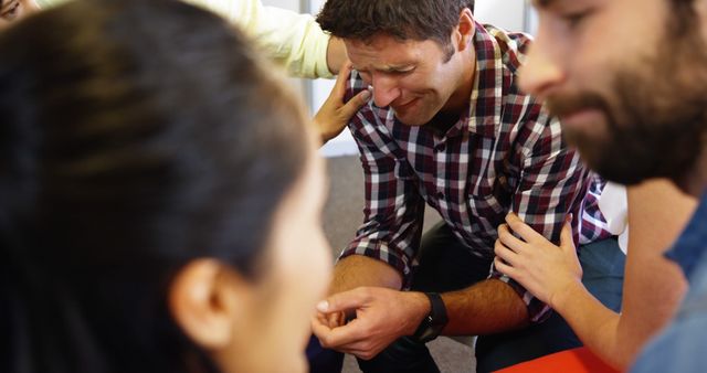 The image depicts a support group session where a distressed man is receiving comfort from other members. This is a powerful scene of empathy and community support, showing people providing emotional assistance through touch and presence. It is useful for illustrating themes of mental health, therapy sessions, counseling, and community support. Can be used in articles or presentations on mental health awareness, therapeutic practices, group counseling techniques, and emotional wellness promotions.