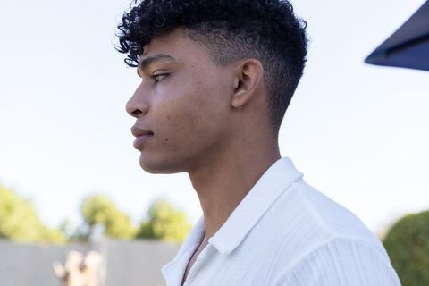 Young african american man standing in profile on sunlit backyard patio wearing white shirt