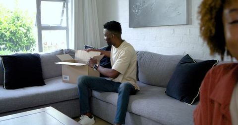 Couple Unboxing Delivery Box on Gray Sofa in Sunlit Living Room