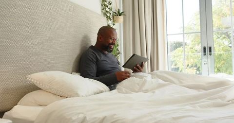 Relaxed Man Enjoying Tablet in Cozy Bedroom with Natural Light