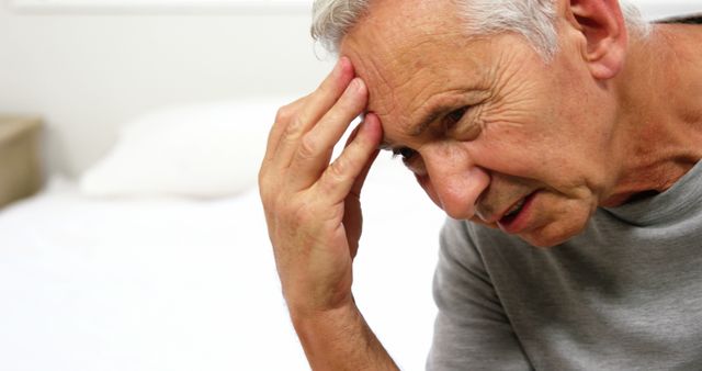 Senior man with gray hair holding his forehead likely experiencing a headache or stress. Useful for topics related to elderly health, stress, pain management, mental health, and healthcare services.