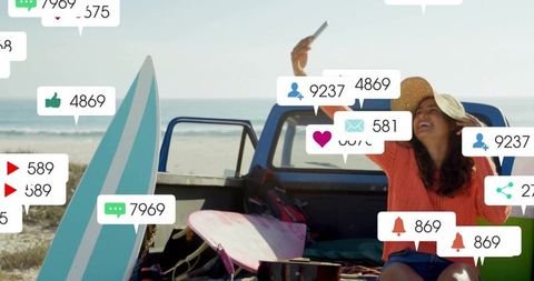 Young woman taking selfie on beach truck tailgate with surfboards and social media alerts