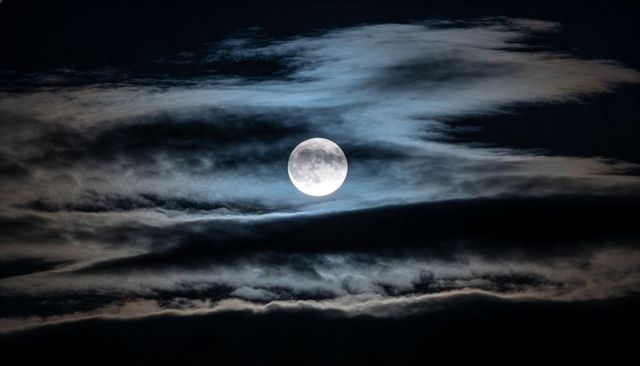 Full Moon Shining Through Layered Clouds Casting Cool Blue Lunar Glow Over Night Sky