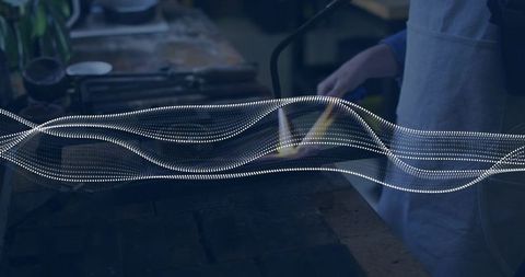 Female glass artist heating torch at workshop bench with flowing dotted light wave overlay