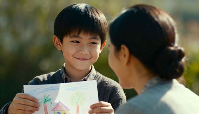 Young boy proudly showing crayon drawing to parent in sunlit park