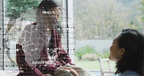 Two Korean women sharing tender moment holding knee by window with hologram globe overlay
