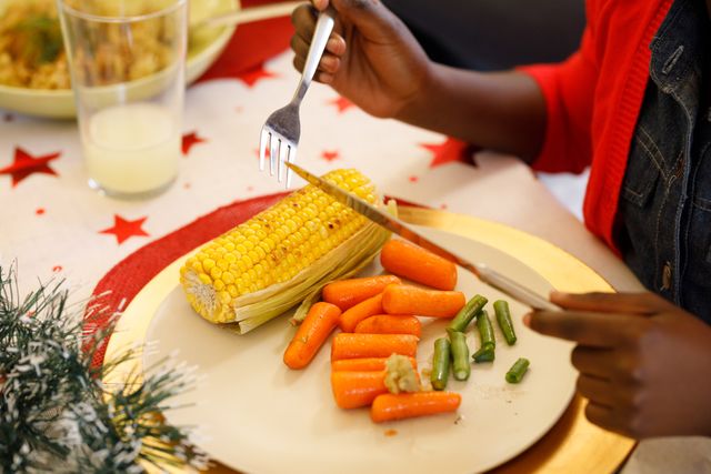 Close up of an african-american child holding a fork and a knife eating at a christmas dinner plate  - Download Free Stock Photos Pikwizard.com