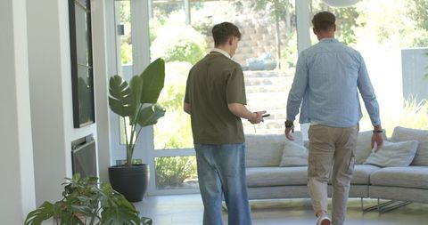 Father and teen walking toward glass door in bright modern living room holding smartphone