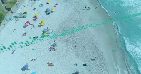 Aerial drone tracking colorful umbrellas along turquoise shoreline with sunbathers and surf