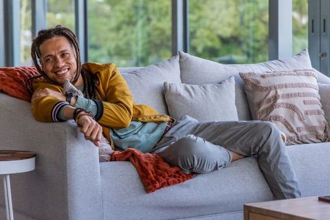 Smiling man reclining on modern sofa in sunlit living room pointing and relaxing