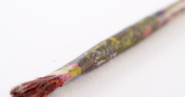 This vibrant close-up shows a well-used paintbrush with dried paint residue on the bristles and handle, ideal for illustrating artistic processes, creativity, and art-focused subjects. Useful for educational materials, art websites, crafting blogs, and creative advertisements.