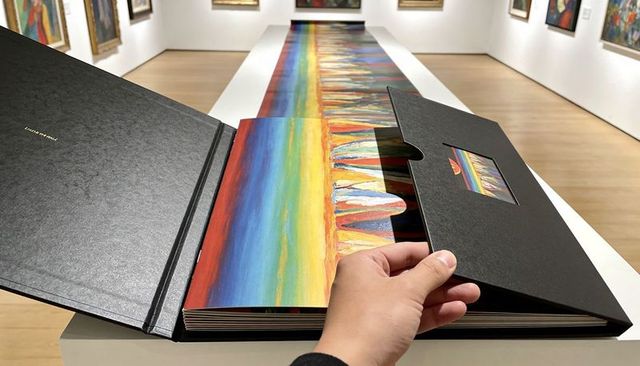 Hand opening black clamshell art book revealing foldout rainbow accordion print gallery