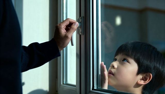 Child pressing face to window glass while adult turning handle, tender quiet home moment