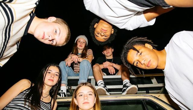 Nighttime teen hangout leaning over vehicle roof laughing talking urban friends