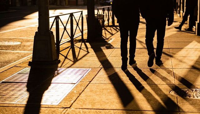 Two pedestrians walking at golden hour casting long dramatic shadows on city sidewalk