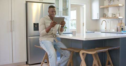 African american man sitting at kitchen island using tablet for remote work and leisure