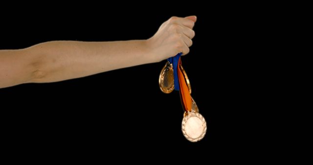 Hand holding gold medals with colorful ribbons on black background. Great for materials about sports achievements, celebrating success, motivation, athletic competition, and award ceremonies.