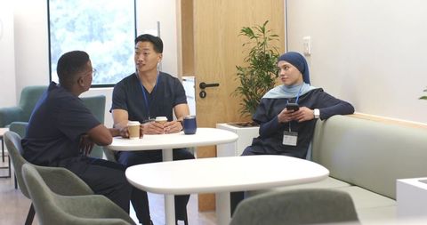 Multicultural healthcare team taking coffee break in bright hospital lounge, collaborating