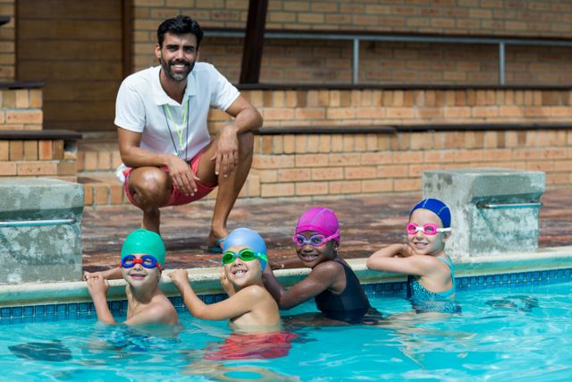 Portrait of happy male trainer with little swimmers at poolside