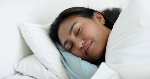 Serene mid-adult asian woman resting on plush white bedding, closeup sleep and comfort