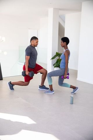 Diverse partners doing weighted lunges in modern living room