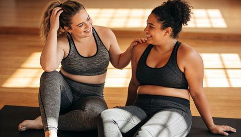 Plus-size friends cooling down after workout, smiling and supporting each other in studio