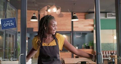 African woman opening glass doors welcoming customers to cozy modern cafe and eatery