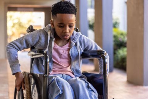 African american preteen boy sitting in wheelchair on sunlit corridor showing resilience