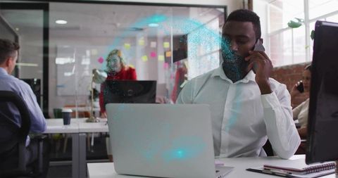 Businessman talking on phone while working on laptop and collaborating in modern open-plan office