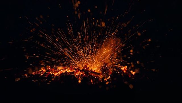 Glowing embers throwing golden sparks over charcoal bed, fiery macro energy burst