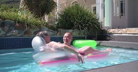 Mature couple floating on pool lounger in sunny backyard conveying calm and companionship