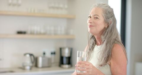 Mature Woman Enjoying Refreshing Glass of Water in Modern Kitchen