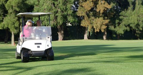 Elderly Couple Driving Golf Cart on Sunny Course