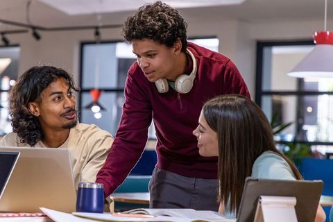 Diverse young team collaborating around laptop planning project in modern coworking hub