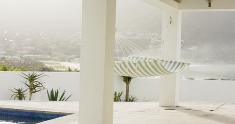 Striped hammock hanging between white columns overlooking misty coastal pool terrace
