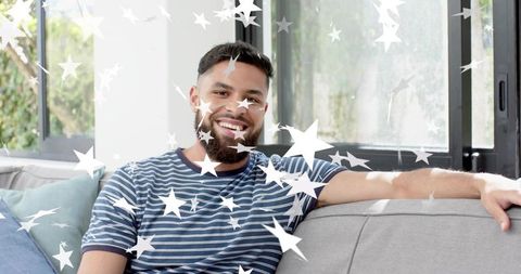 Smiling young man relaxing on sofa with star decals in sunlit modern living room