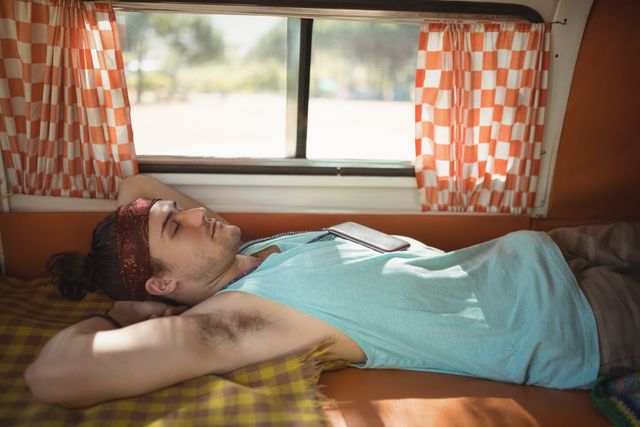 Young man resting in a van by the window, embodying a relaxed and carefree lifestyle. Ideal for use in travel blogs, adventure magazines, and lifestyle advertisements promoting road trips, vacations, and outdoor leisure activities.