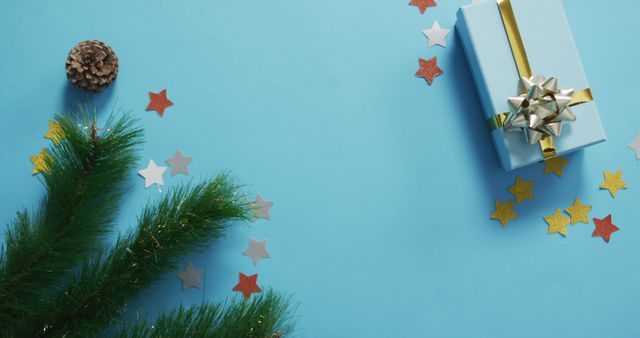 Charming Christmas scene featuring a wrapped gift with a golden ribbon, green pine branches, and star-shaped confetti on a blue background. Ideal for holiday greeting cards, festive invitation designs, or winter promotional material.