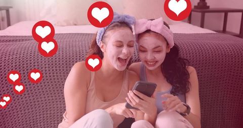 Friends sharing at-home spa night, sending hearts on phone while wearing sheet masks