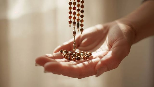 Cradling hands holding amber beaded necklace in warm window light closeup soft bokeh