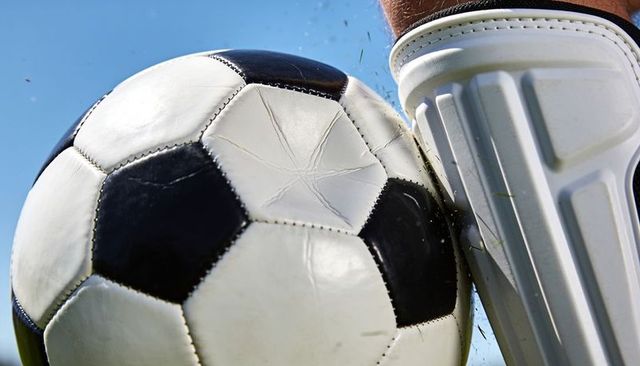 Close-up soccer ball struck by player shin guard, flying grass and dynamic impact