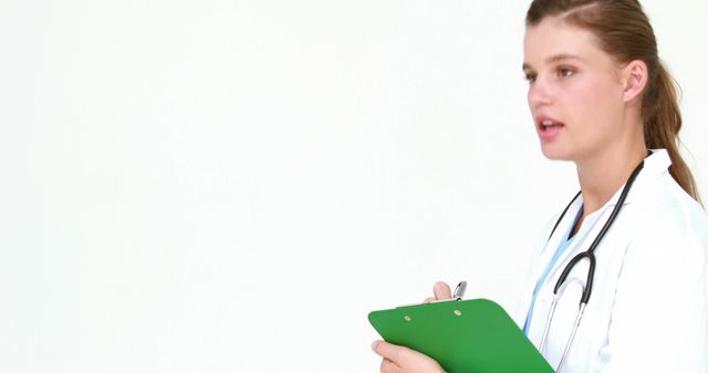 A young Caucasian female doctor is holding a clipboard, with copy space. Her focused expression and professional attire suggest she is reviewing patient information or preparing for a consultation.